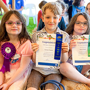Three children hold certificates after winning colouring competition
